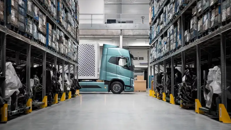 Electric truck in teal parked inside a large warehouse distribution centre